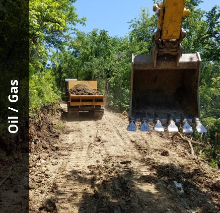 Excavator following a dump truck down an access road | Oil / Gas Excavating Services